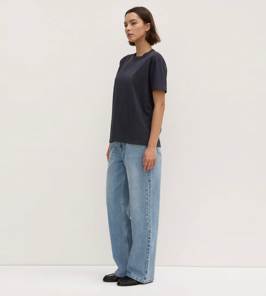 Woman wearing a dark blue t-shirt and light blue jeans against a white background