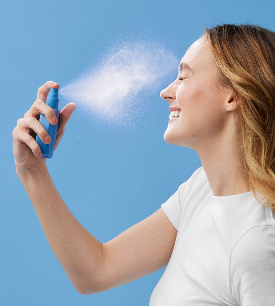 Woman using a blue spray bottle against a clear blue sky