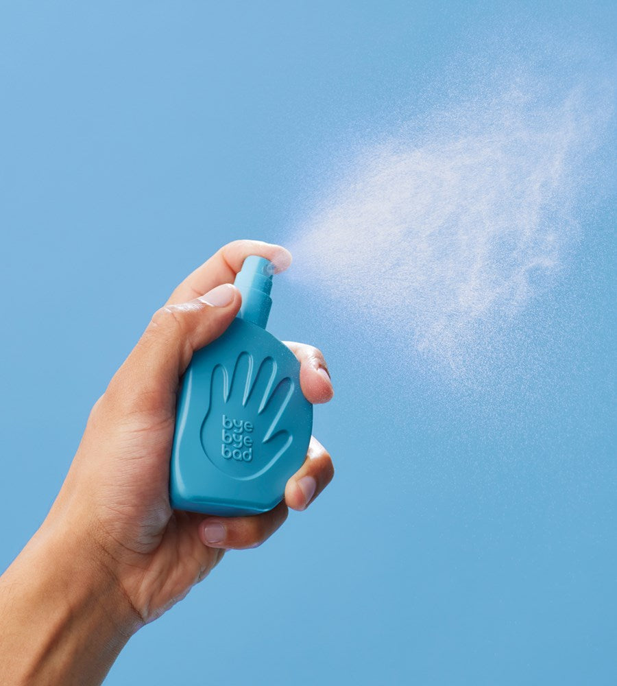Hand holding a blue spray bottle against a clear blue sky