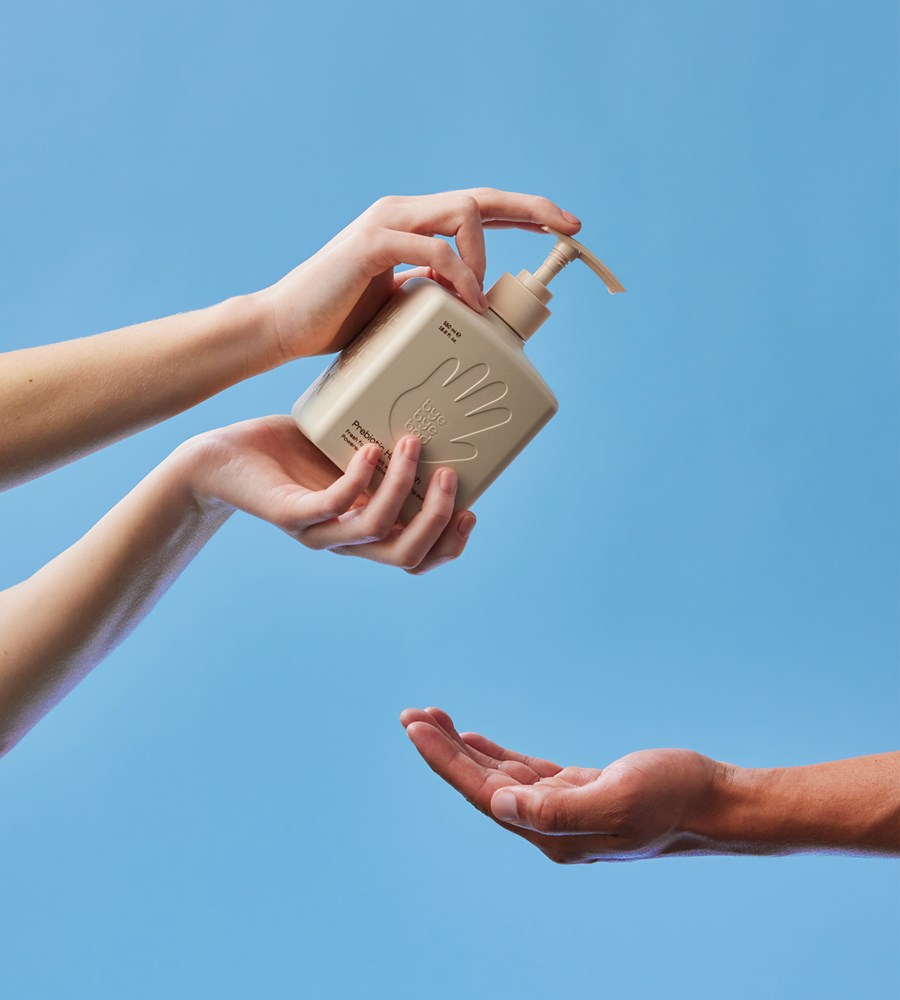 Hand holding a beige hand sanitizer bottle with pump against a blue background