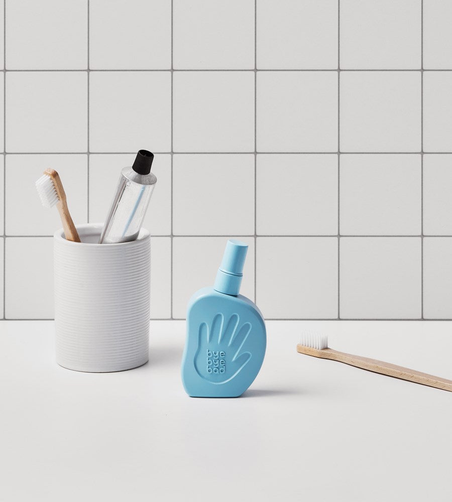 Blue bottle with hand design on a bathroom counter next to a white cup with toothbrushes and a bottle.