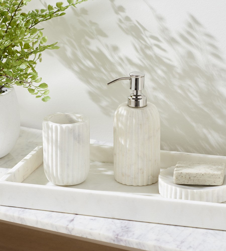 White ceramic soap dispenser on a marble surface with a plant in the background