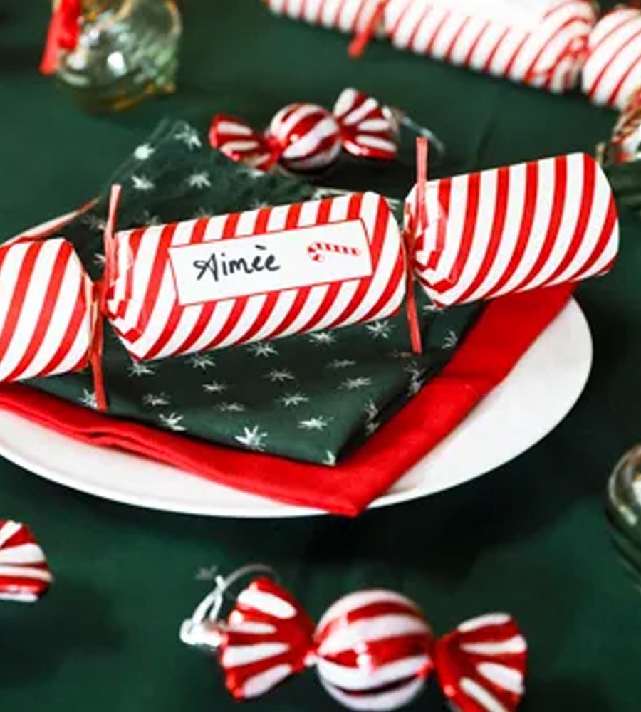 Decorative Christmas cracker with striped paper and a name label on a festive table setting.