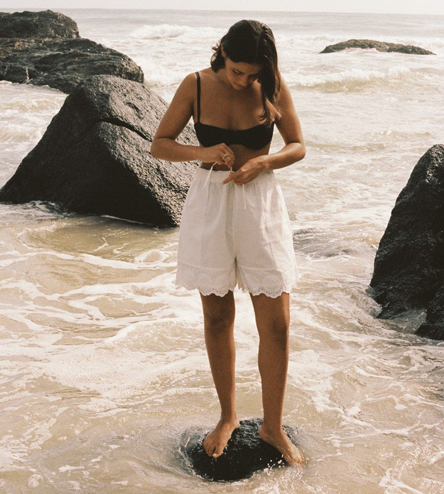 Woman standing on a rock in the ocean with large rocks and water in the background