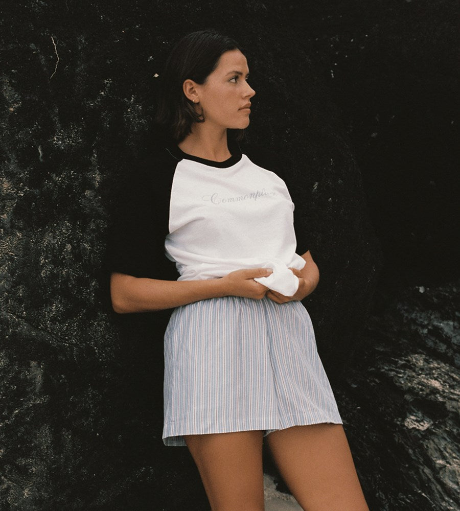 Woman wearing a white and black baseball shirt and striped shorts against a dark background