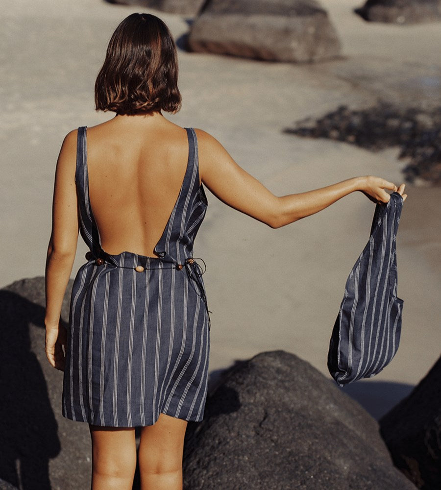 Woman in a striped dress holding a matching bag on a beach.