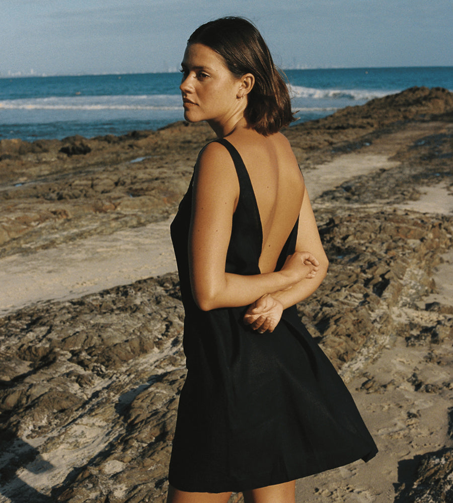 Woman in a black dress standing on a rocky beach with ocean view