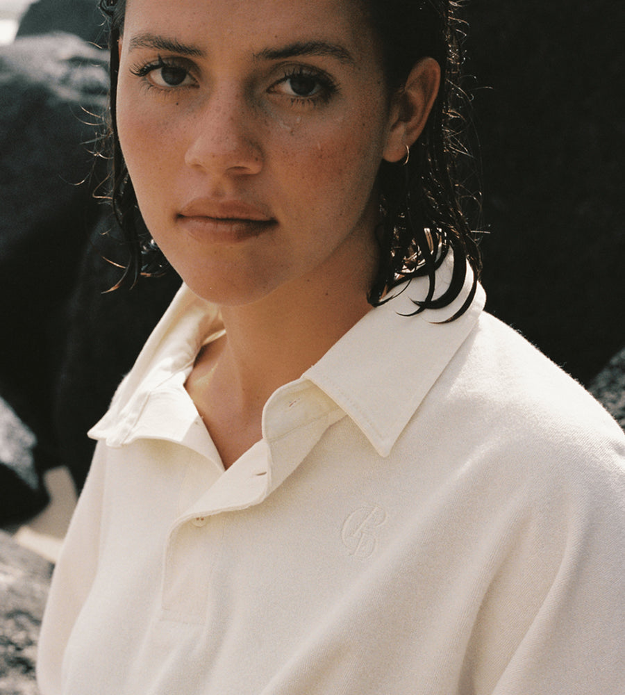 Person wearing a white shirt with a brand logo, standing against a dark background