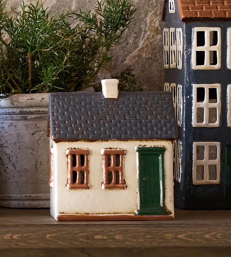 Small ceramic house model on a wooden surface with a plant in the background