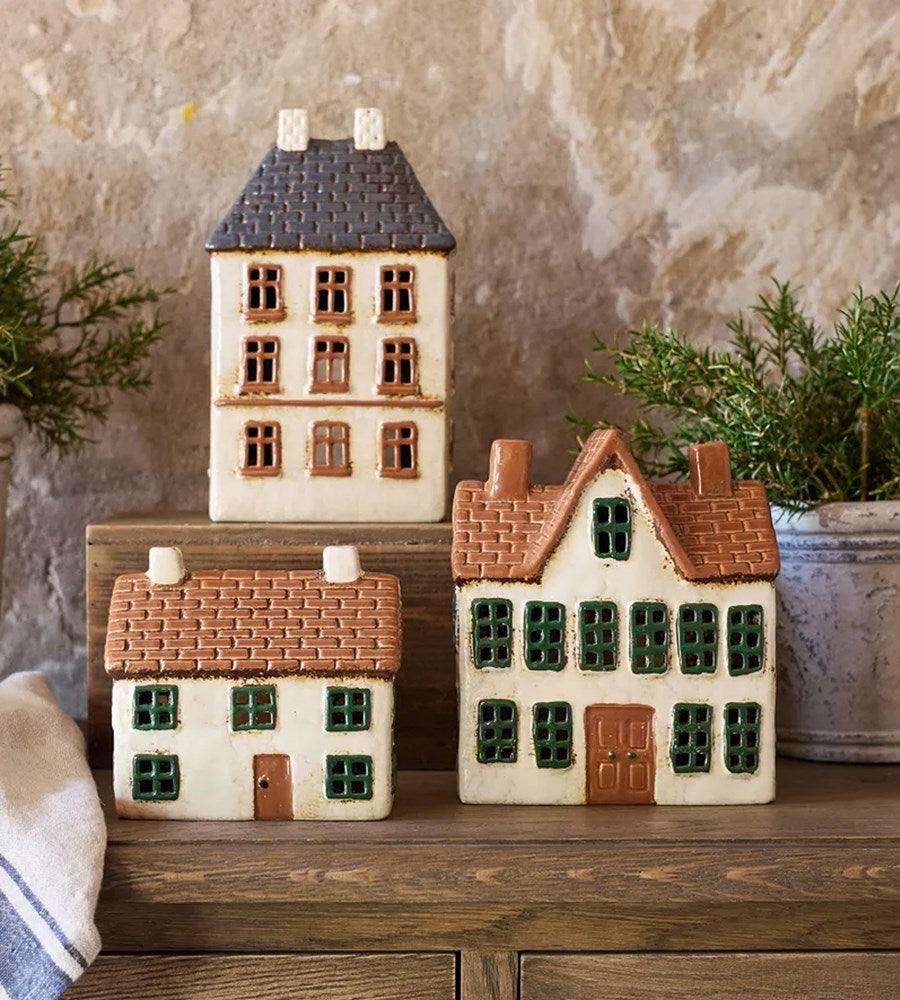 Set of ceramic house-shaped decorative items on a wooden surface with a neutral background.
