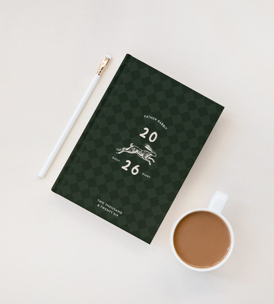 Green checkered notebook with a pen and coffee cup on a white surface