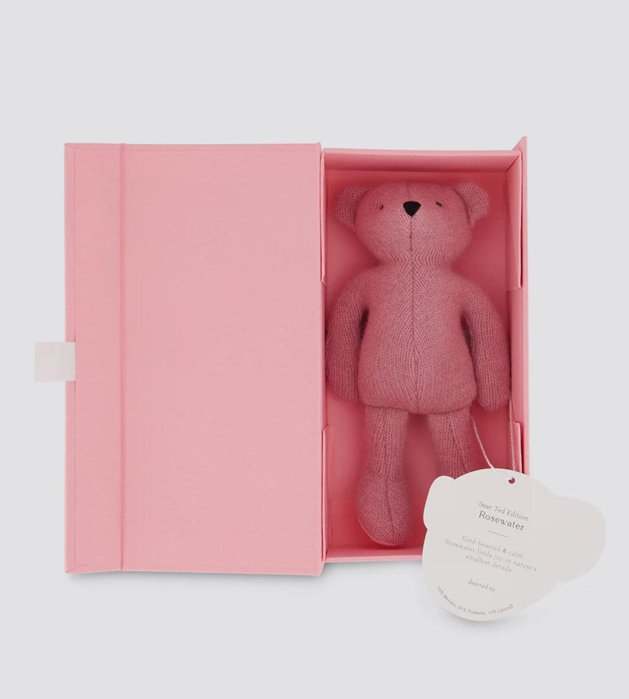 Pink teddy bear in a pink box with a heart-shaped tag on a light gray background