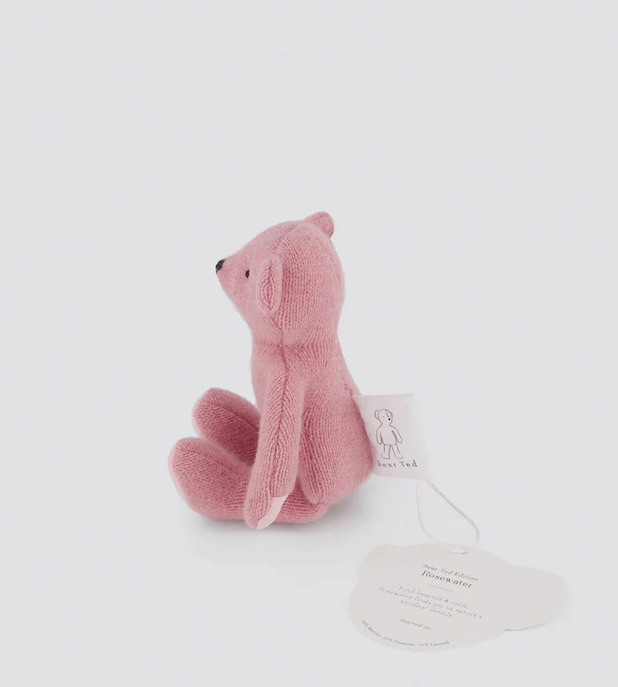Pink knitted toy bear with a tag on a white background