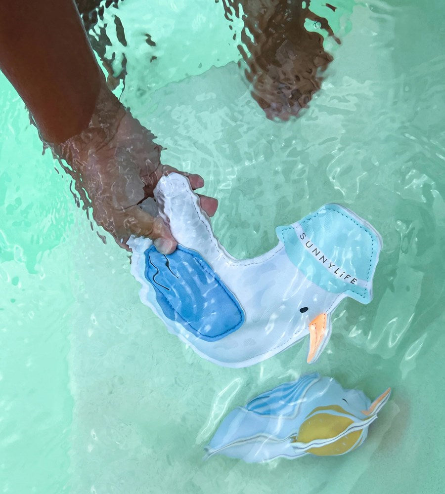 Person holding a blue and white toy in a pool with another similar toy on the bottom right corner.
