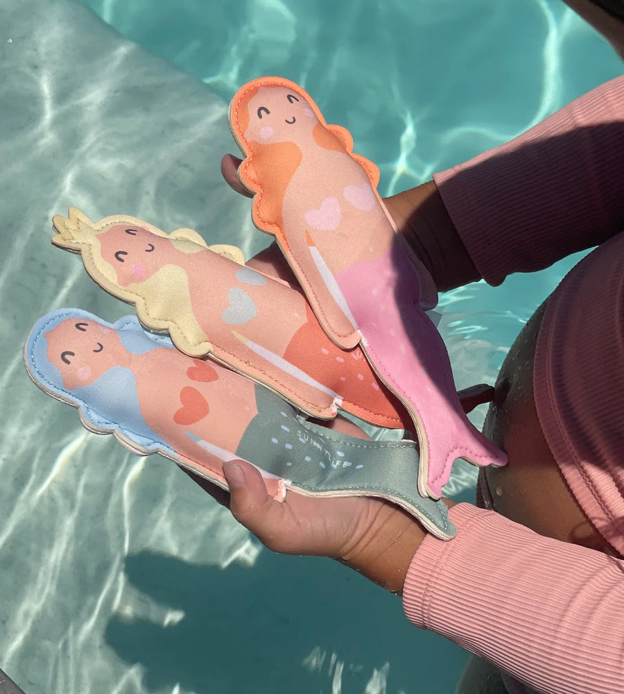 Person holding mermaid-shaped slippers with a pool in the background