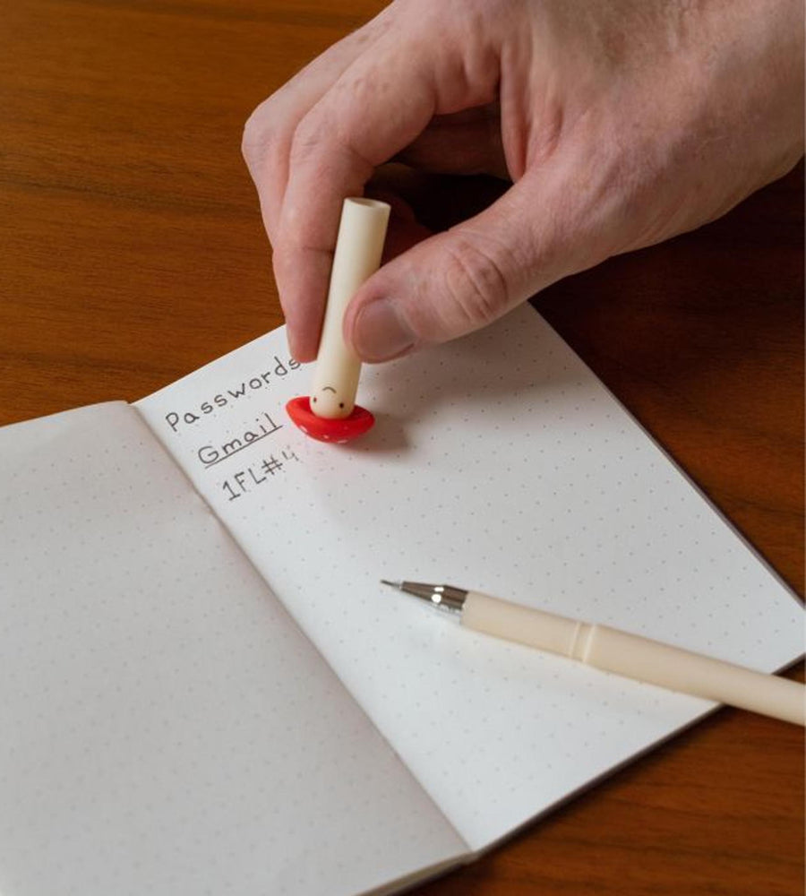 Hand holding a small cylindrical object over a notebook with password entries on a wooden surface.