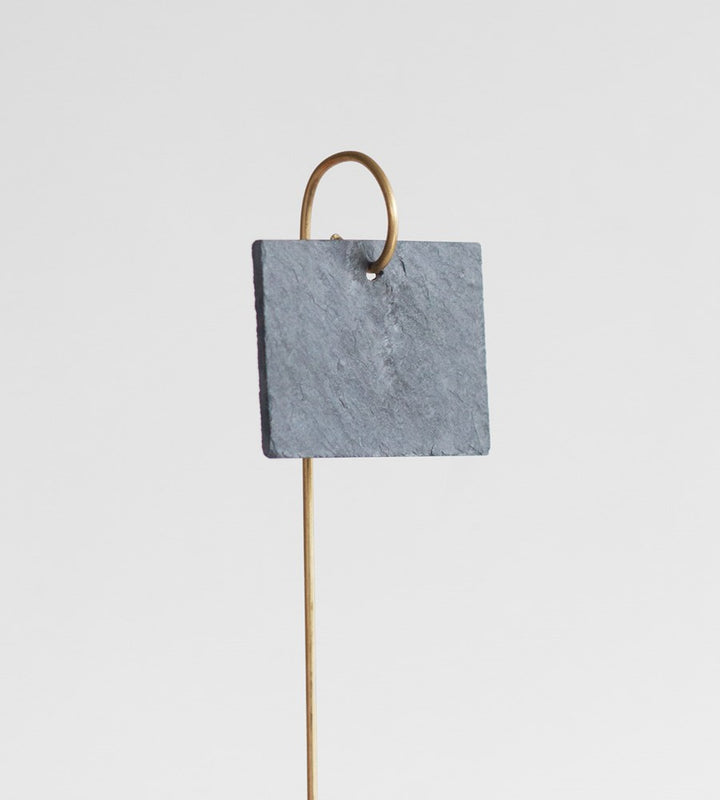 Decorative item with a square gray stone and gold metal rod on a light gray background