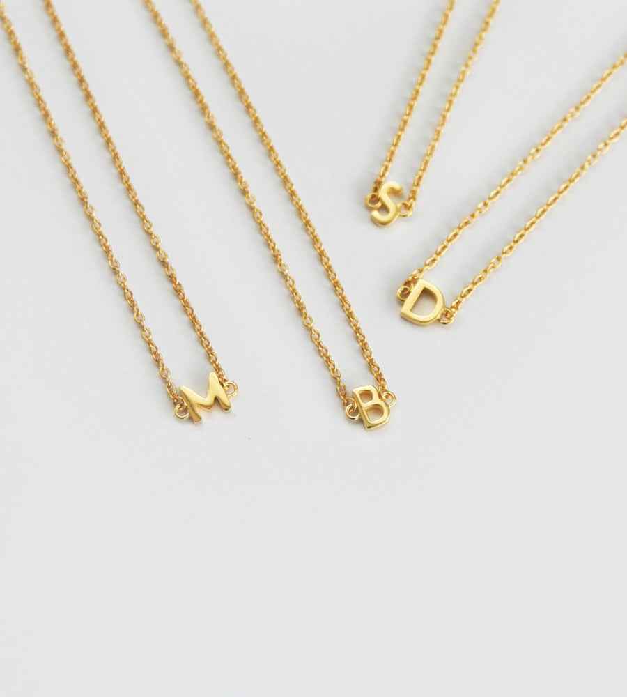 Three gold necklaces with letter pendants on a light gray background