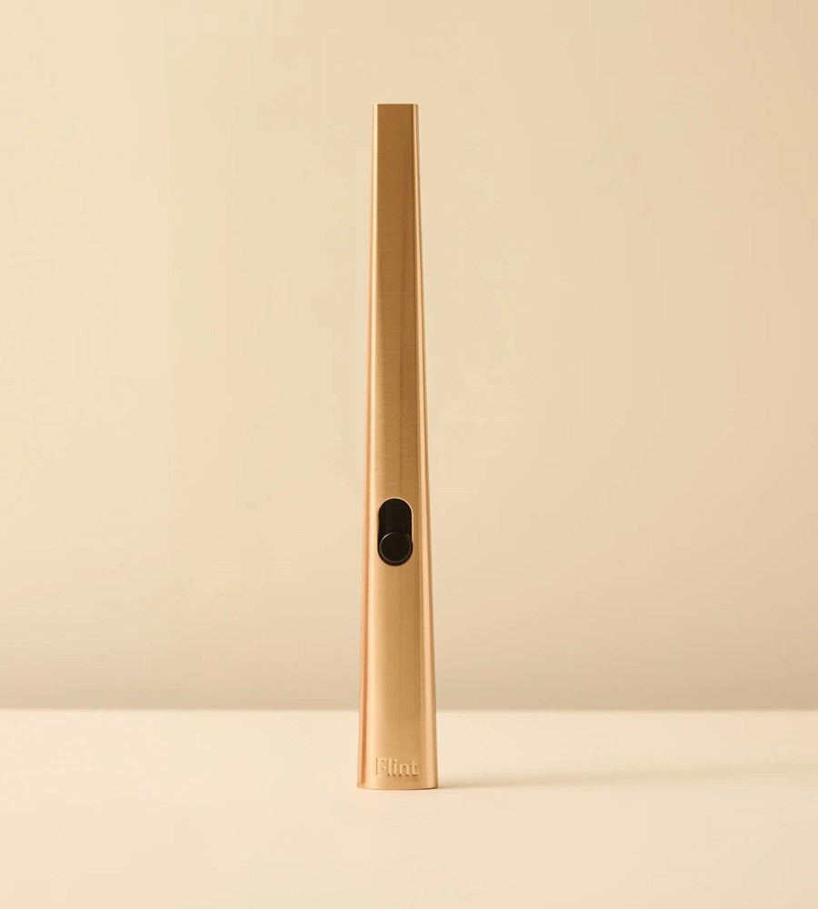 Gold cylindrical object with a brand logo on a beige background