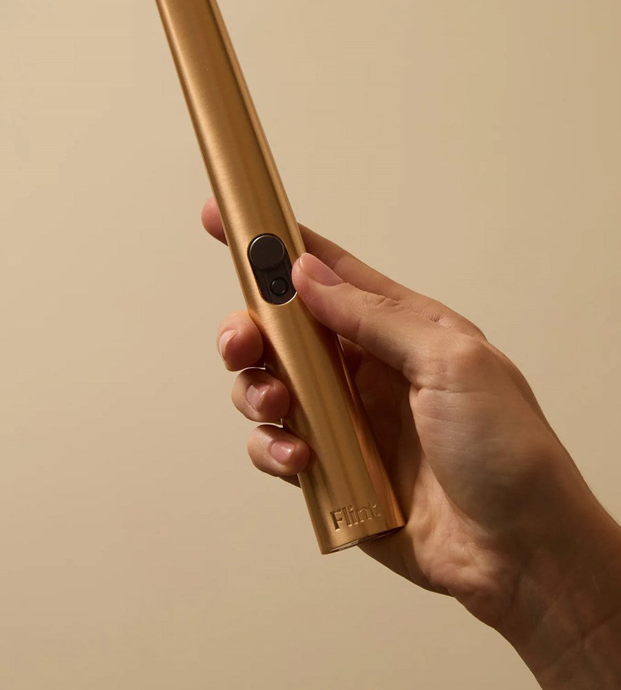 Hand holding a gold cylindrical device with 'Fiat' branding against a beige background