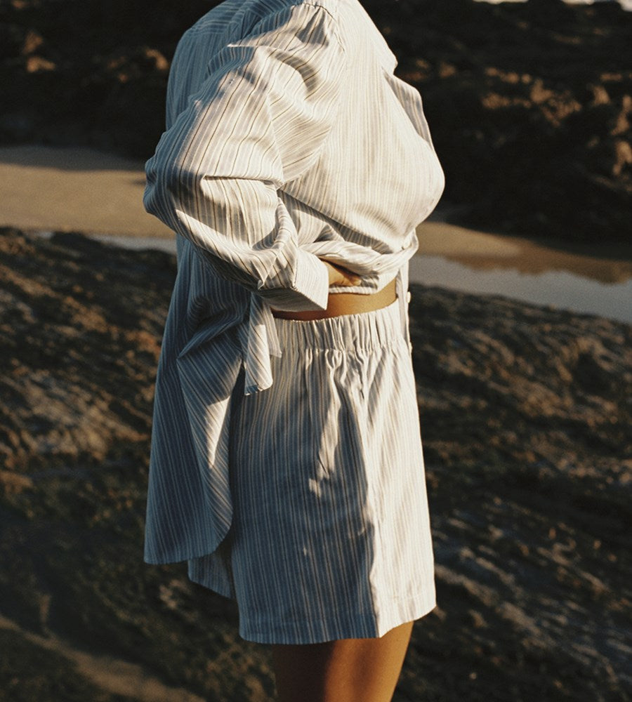 Person wearing a light-colored dress with a hood in a natural setting