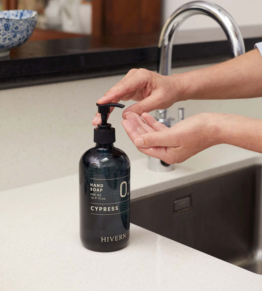 Person using a bottle of Hivern Cypress hand soap on a kitchen counter.