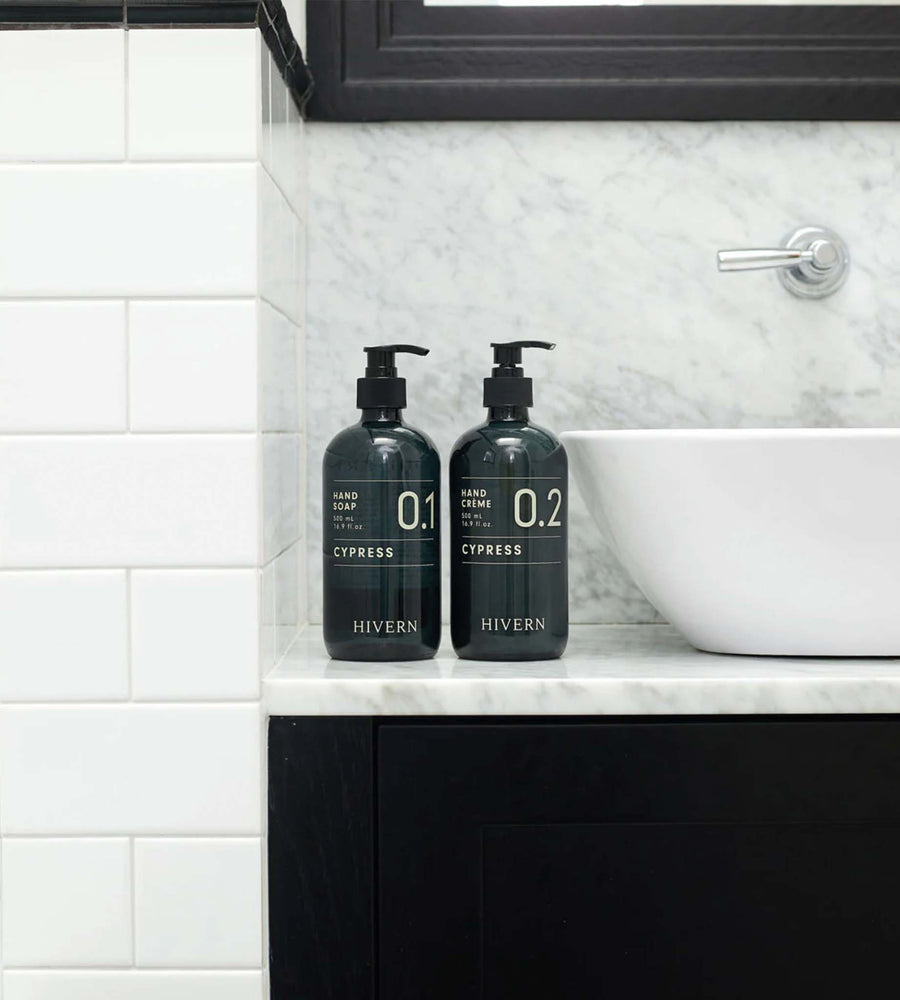 Two black bottles labeled 'Hivern' on a bathroom counter with a marble backsplash.