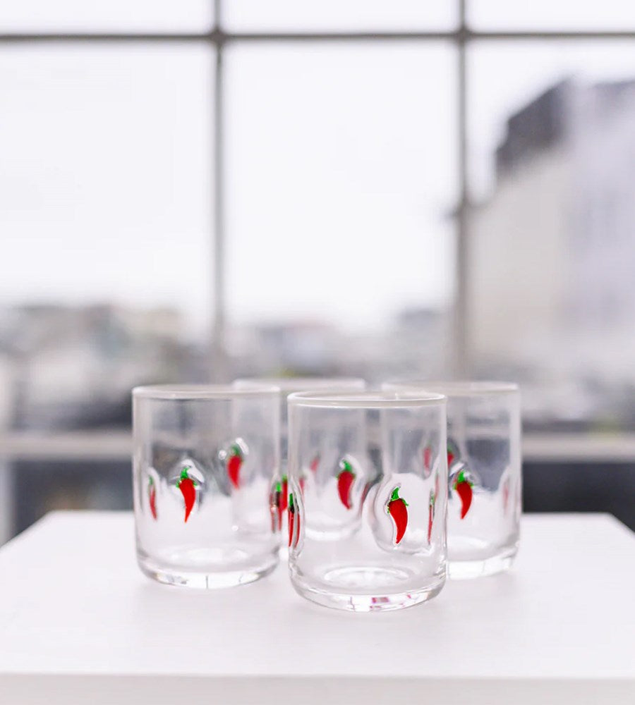 Set of four glass tumblers with red chili pepper design on a white surface.
