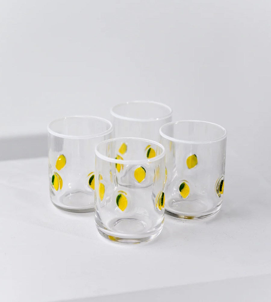 Four glass tumblers with lemon design on a white surface