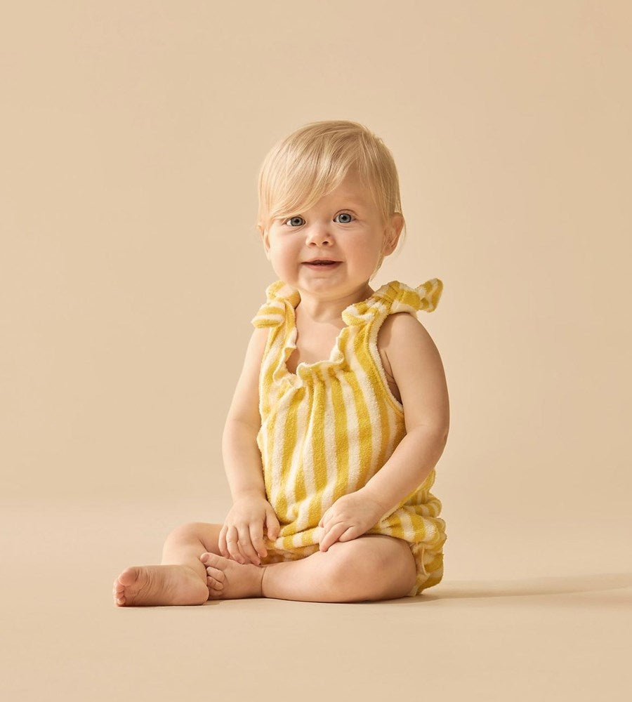Baby wearing a yellow striped romper sitting on a beige background