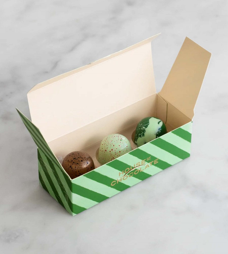 Green striped chocolate box with three chocolate eggs on a marble surface