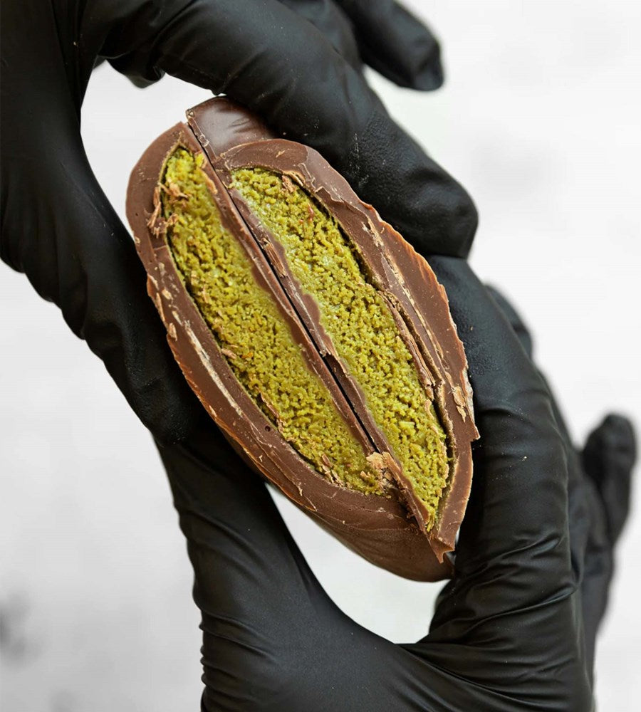 Chocolate-dipped green matcha cookie held by a gloved hand against a neutral background