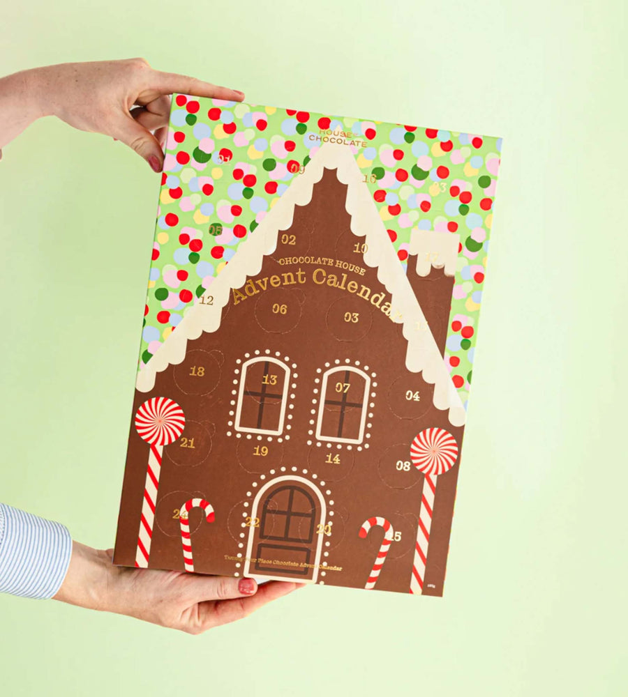 Gingerbread house-shaped advent calendar held by a person against a light green background