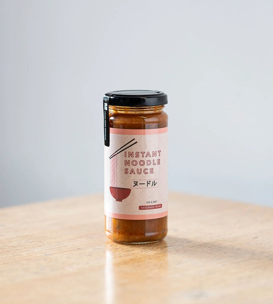 Jar of instant noodle sauce on a wooden surface with a light gray background