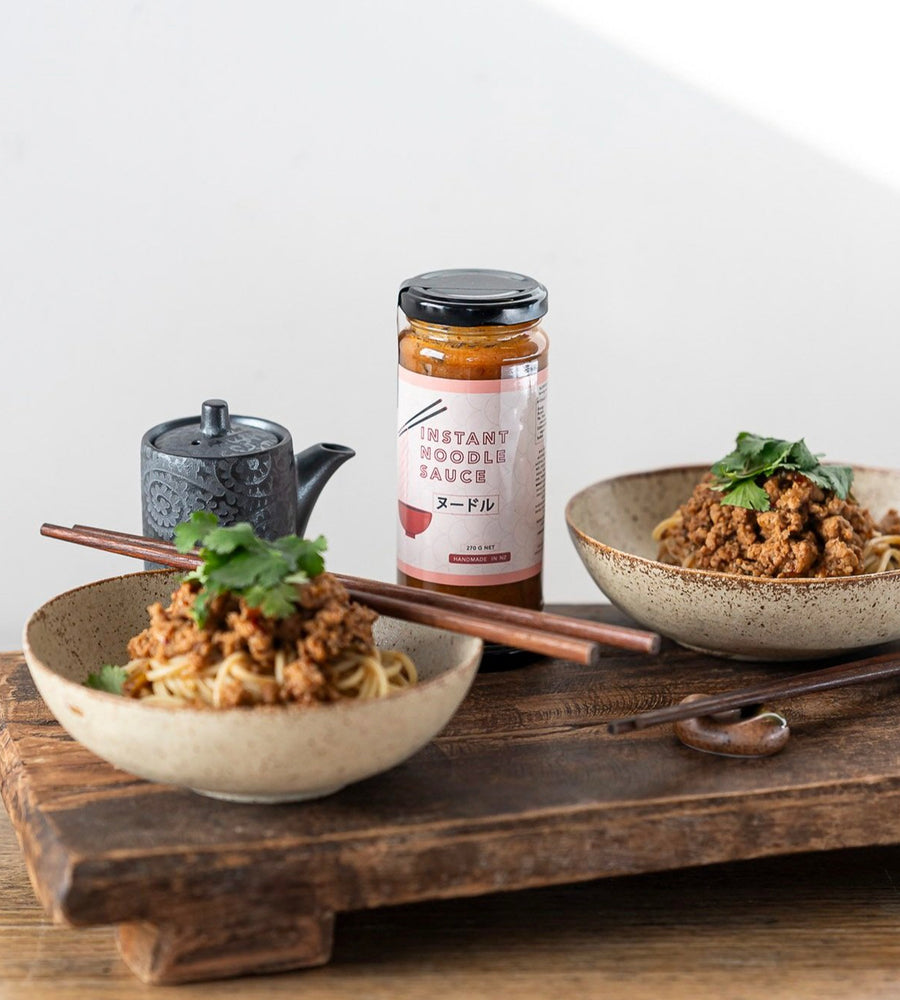 Two bowls of food with a bottle of instant noodle sauce on a wooden tray.