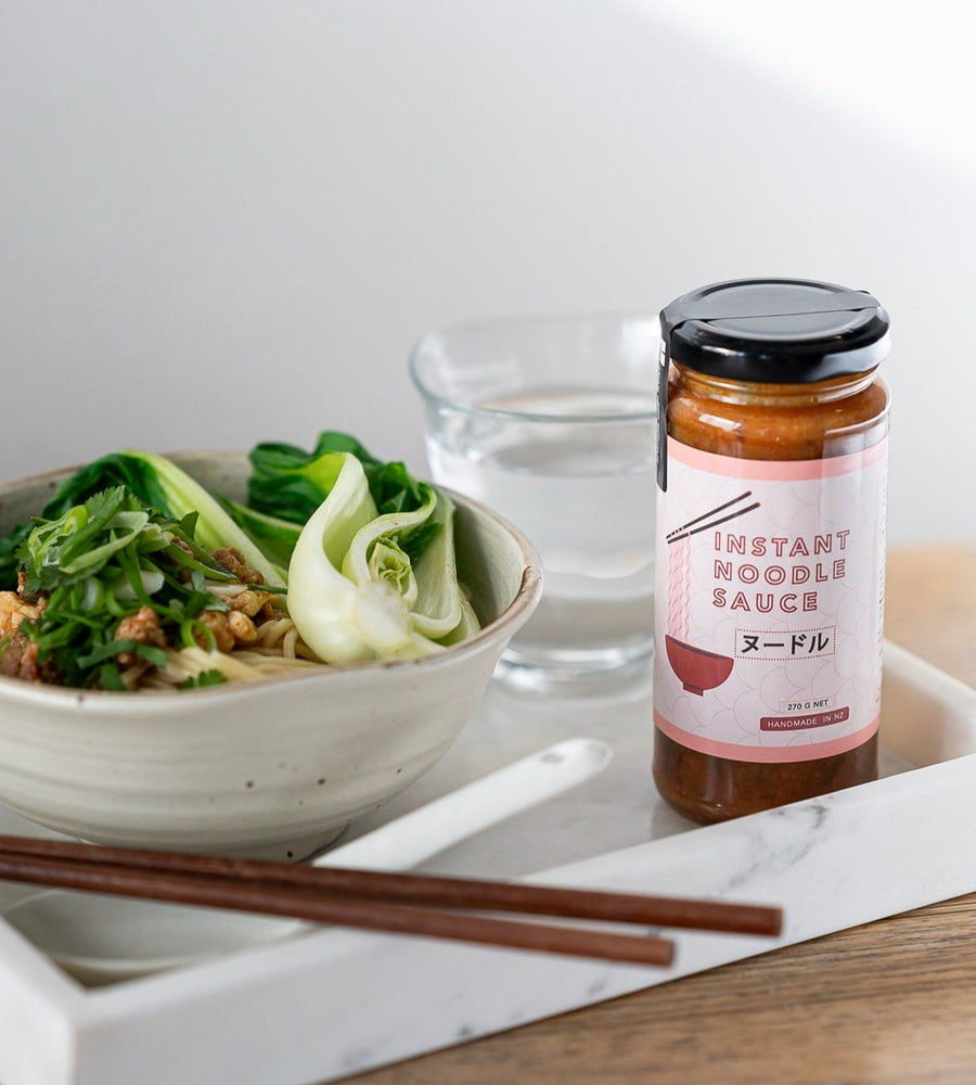 Bowl of noodles with a bottle of instant noodle sauce on a marble surface