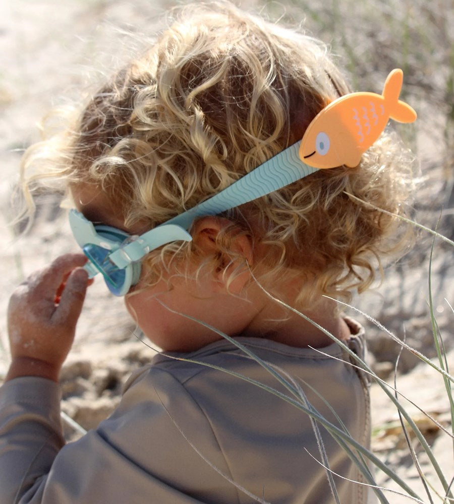 Child wearing a blue swim mask with a fish design on a beach