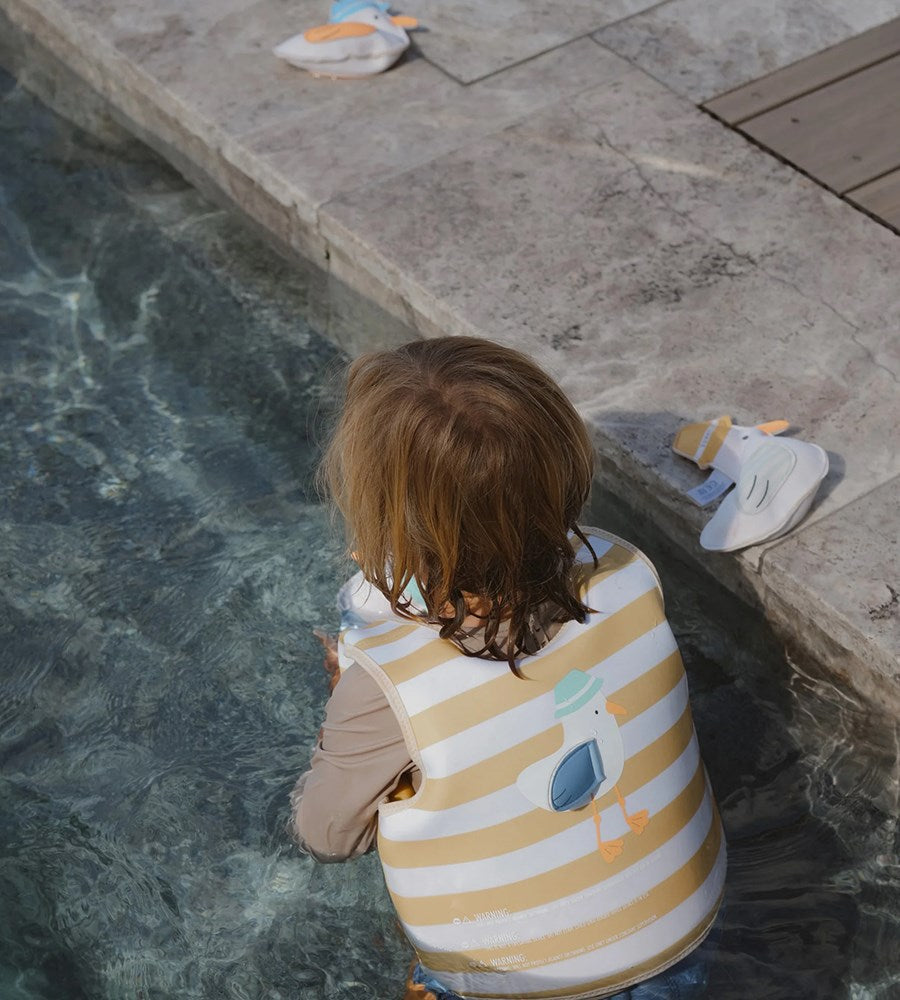 Child wrapped in a striped towel by a poolside with a toy duck nearby