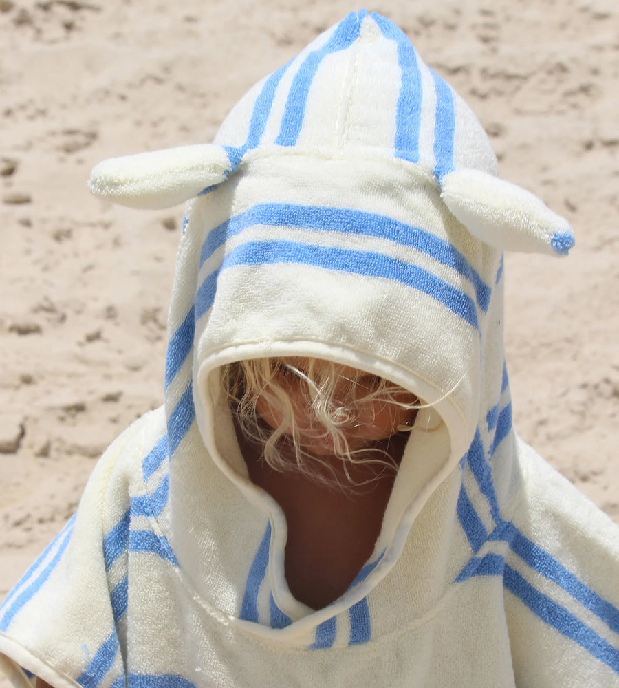 Child wearing a white hooded towel with blue stripes and animal ears on a sandy background