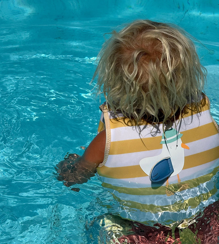 Child in a striped swimsuit with a boat design, standing in clear blue water.