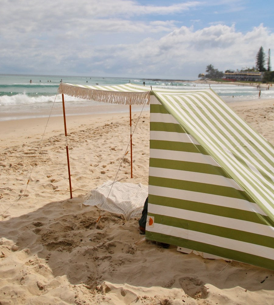 Green and white striped beach tent on a sandy beach with ocean view