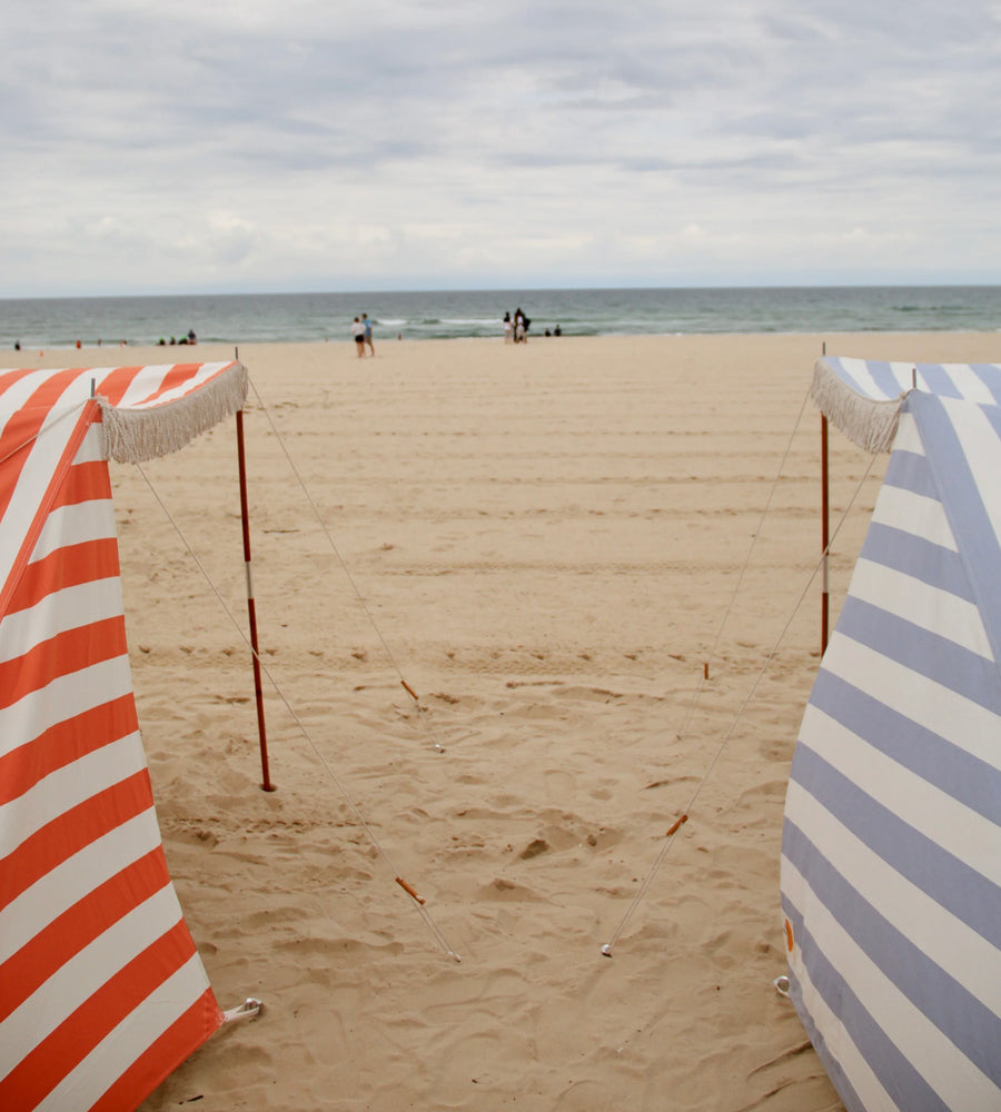 Two striped beach chairs on a sandy beach with ocean and sky in the background.