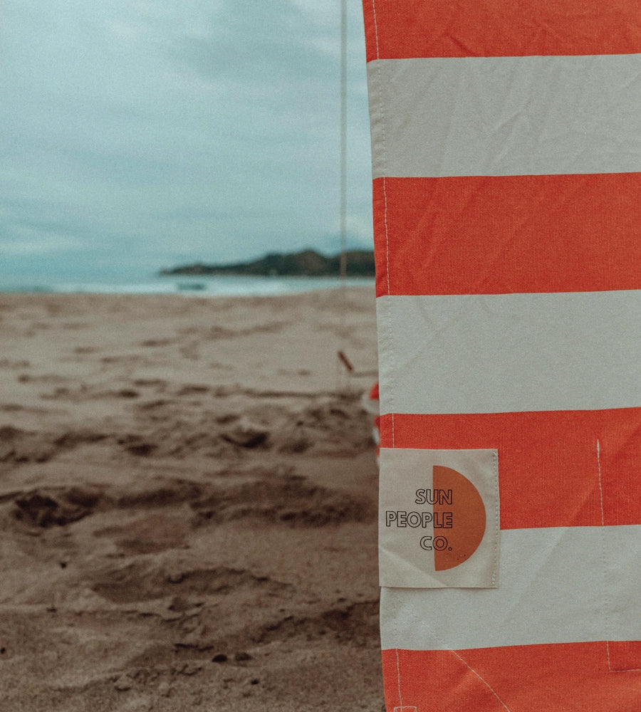 Orange and white striped flag with 'Sun People Co.' logo on a beach