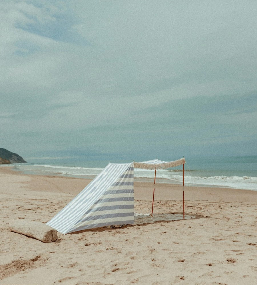 Beach umbrella with striped cover on a sandy beach with ocean and sky in the background
