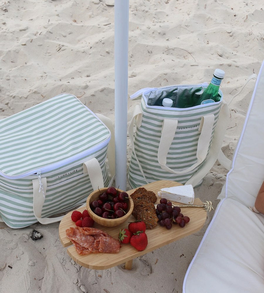 Beach setting with striped cooler bags, a small table with food, and an umbrella on sandy ground.