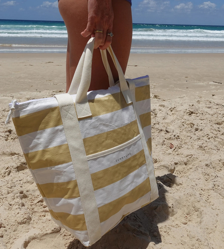 Striped beach bag held by a person on a sandy beach with ocean waves in the background