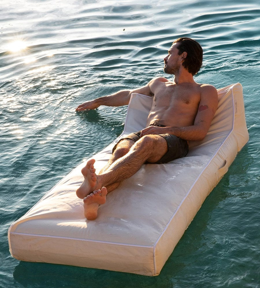 Man relaxing on a floating inflatable mattress in the water.