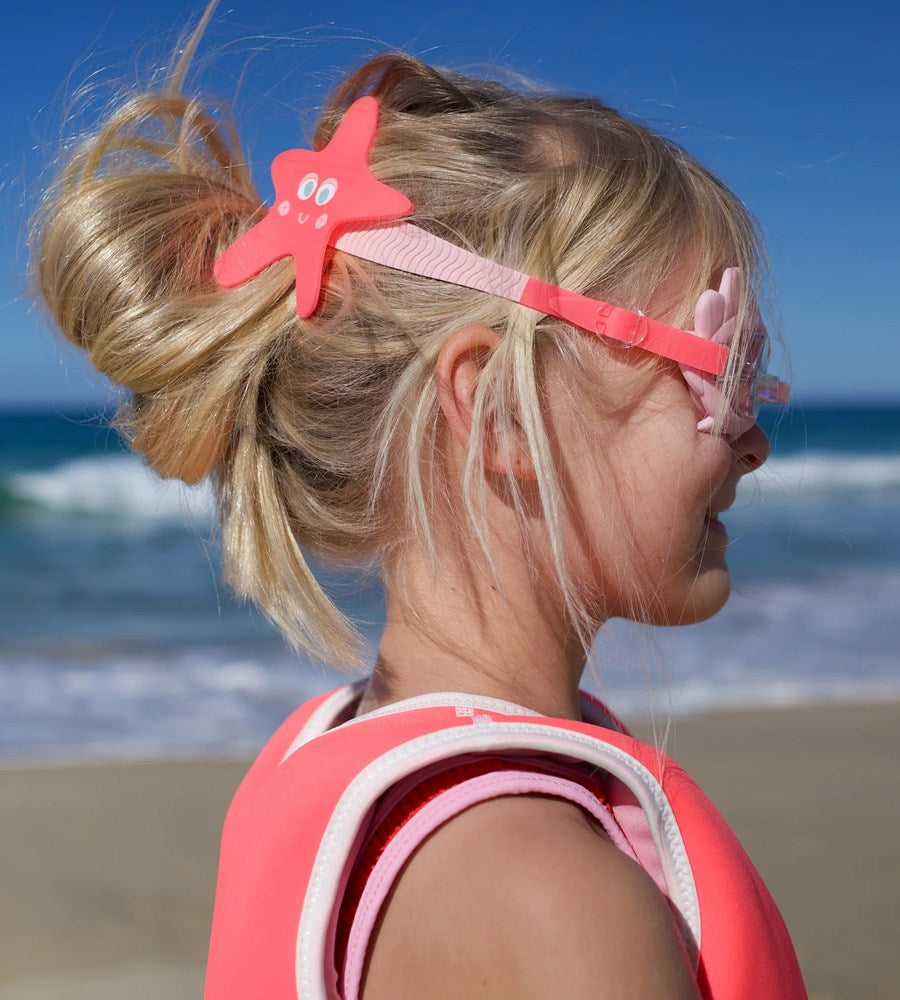 Child with starfish hair clip and sunglasses on a beach