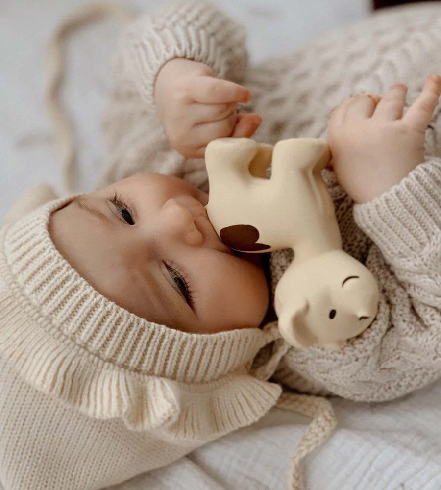 Baby in a knitted outfit holding a soft toy, wearing a matching hat.