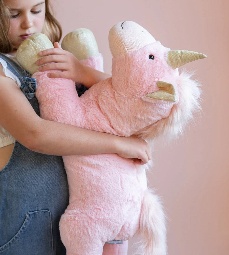 Child holding a pink unicorn plush toy against a pink background